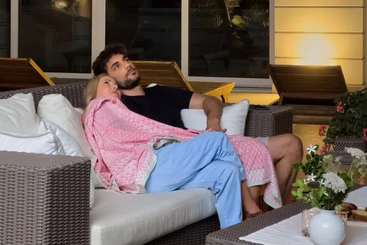 Abby and Theo snuggling on a cozy outdoor couch under a pink blanket, looking up at the stars.