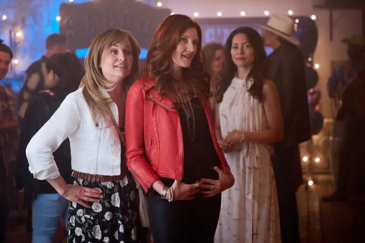 Three women standing indoors, one wearing a red jacket and the others in casual attire. From Hallmark's "Big Sky River: The Bridal Path" 