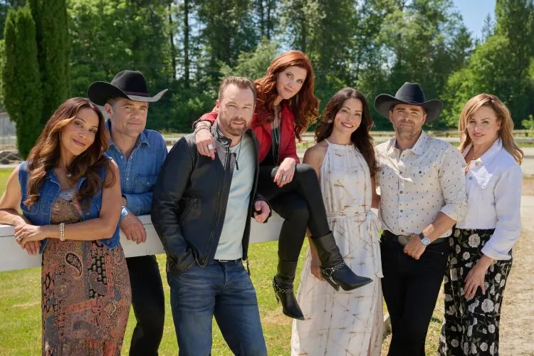 A group of seven people standing outside, posing together for a group photo by a fence. From Hallmark's "Big Sky River: The Bridal Path" 
