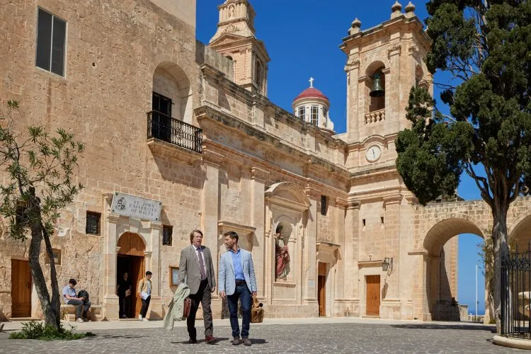 Two men walking and talking in front of a historic building. From Hallmark's "For Love & Honey"
