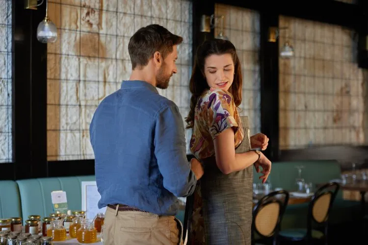  A man helping a woman adjust her clothing in a cozy restaurant setting.
