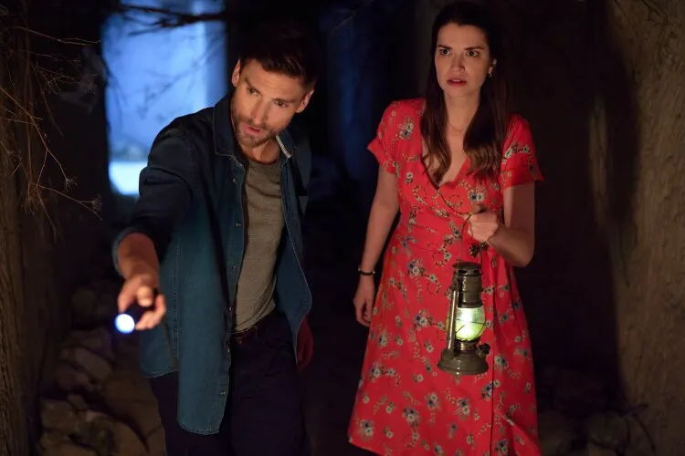 A man and a woman exploring a cave, holding a lantern and a flashlight.