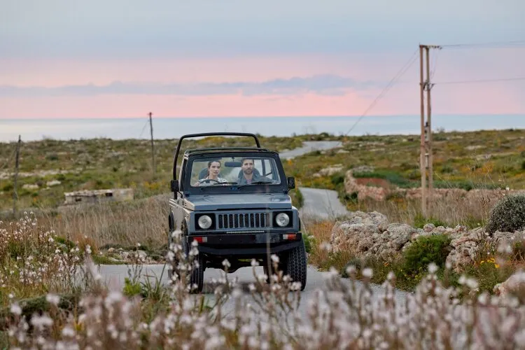 A man and a woman driving in a jeep on a scenic road at sunset. From Hallmark's "For Love & Honey"
