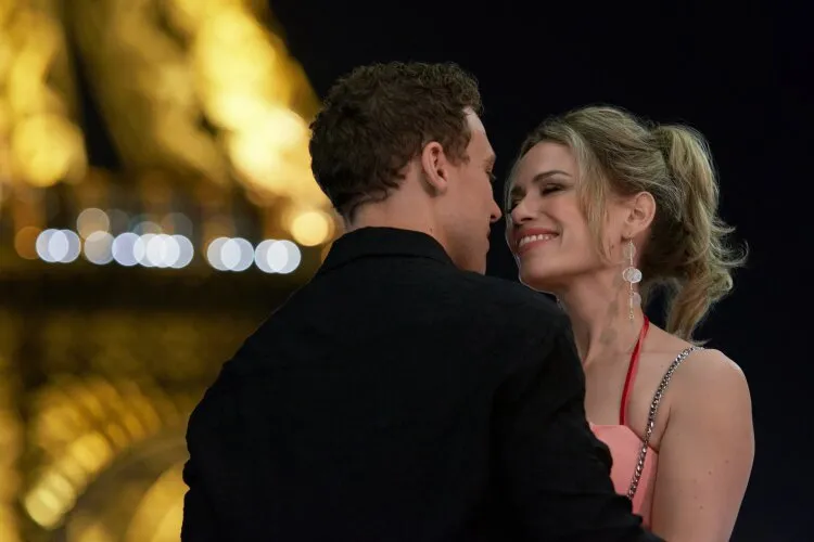 A couple dancing and smiling at each other in front of the illuminated Eiffel Tower at night.
