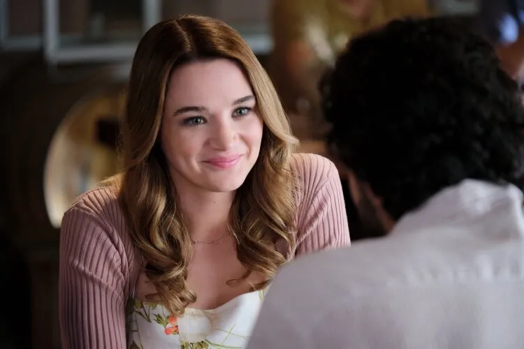 A woman with long brown hair smiling warmly at a man during a conversation in a cozy setting.