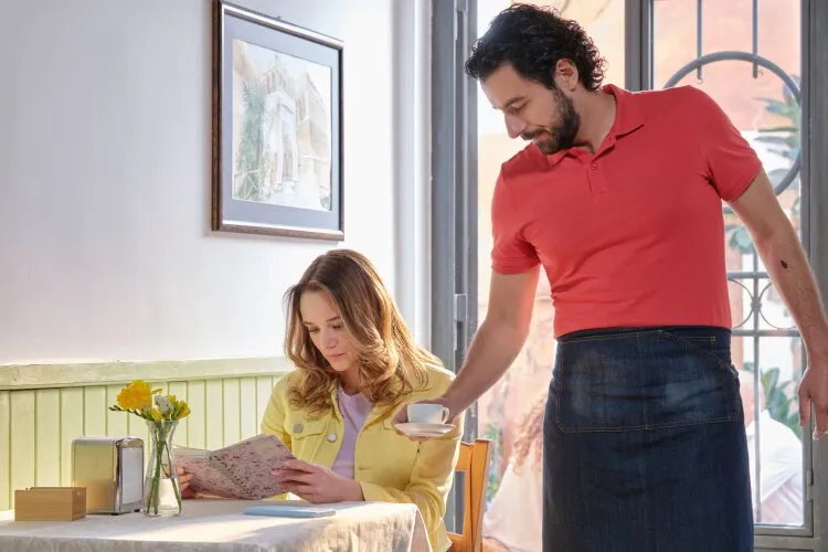 A waiter serving a woman at a café table, both smiling as she looks at the menu. "Two Scoops of Italy"  on Hallmark.