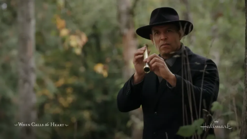 Secretive Observation: A man in a dark coat and hat explores the woods his expression serious and focused, adding a layer of mystery and intrigue to the scene. "Run to You When Calls the Heart"