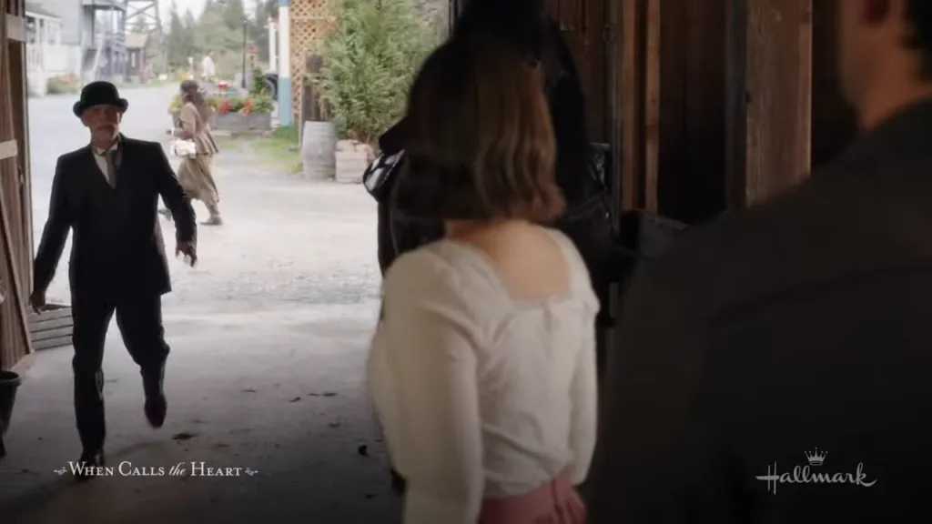 Old man entering a barn: An elderly man in a black suit energetically enters a barn where Elizabeth Thatcher is standing with a subdued expression. "Run to You When Calls the Heart"