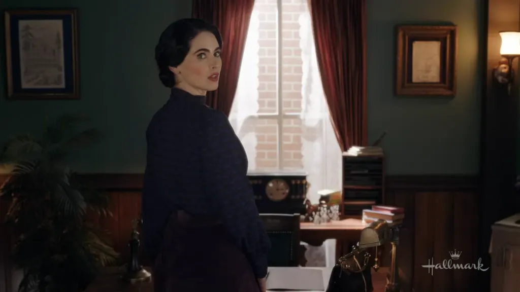 A woman dressed in a blue blouse and brown skirt, stands in her office, looking over her shoulder with a surprised expression.