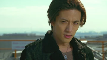 Takumi Inui from Kamen Rider, dressed in a dark jacket, stands with a serious expression. The background features a cityscape bathed in soft sunlight, adding a sense of depth and intensity to the scene.