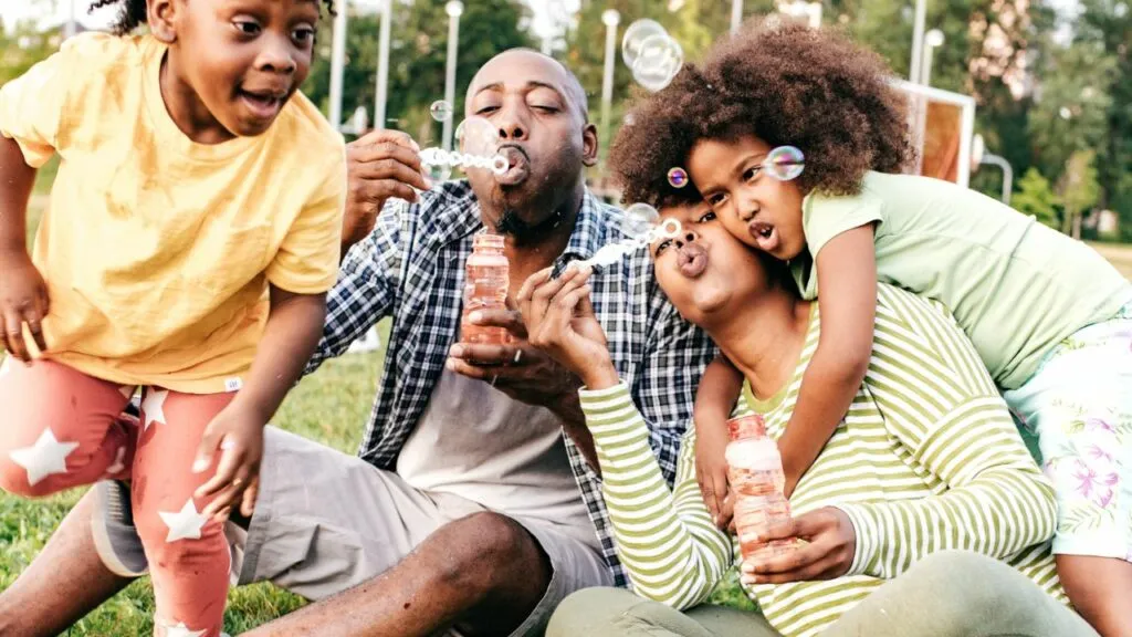 A joyful image emphasizing the importance of incorporating physical activity into homeschooling routines. A family is seen enjoying outdoor fun by blowing bubbles together in a park, highlighting the value of fresh air, exercise, and play. This visual serves as a reminder to balance academic work with physical activity to keep homeschooling engaging and promote overall well-being.