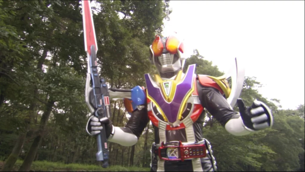 A scene from the Tokusatsu series featuring Kamen Rider Den-O. The character is in full armor, showcasing a vibrant and colorful design. The suit features a mix of red, purple, yellow, and silver elements, with a striking chest plate that has a large purple "V" shape. The helmet has large, multifaceted orange eyes resembling those of an insect, specifically a butterfly. The character is holding a large weapon, a combination of a sword and a gun, adding to the formidable appearance. The background consists of a wooded area with trees and greenery, contrasting with the futuristic and flamboyant design of the Kamen Rider. The overall scene captures the dynamic and heroic essence of Kamen Rider Den-O, ready for action in a natural setting.