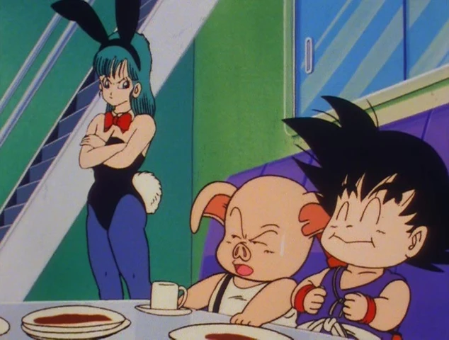 A humorous moment from Dragon Ball featuring Bulma, Oolong, and Goku. Bulma stands in the background wearing a bunny costume with a frustrated and annoyed expression, arms crossed. Oolong, seated at the table, looks unimpressed, holding a small cup of tea. Goku, next to him, is grinning happily, seemingly oblivious to the tension. Plates of food are spread out on the table in front of them, adding to the lighthearted atmosphere. The setting is a retro-styled interior, with bright green walls and a glass-paneled staircase in the background. Classic Dragon Ball charm on display!