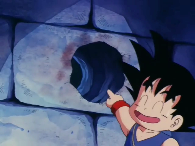 Goku smiles proudly, pointing to a small hole he created in a stone wall with his Kamehameha, showcasing his success in breaking through the barrier.