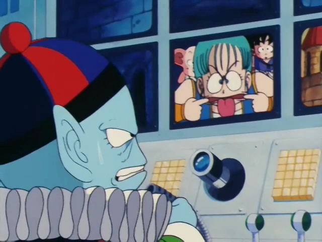 Emperor Pilaf, sweating and frustrated, sits at his control panel while a monitor shows Bulma making a mocking face, sticking out her tongue and pulling her cheeks. Goku, Oolong, and Yamcha are visible in the background of the monitor.