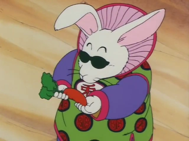 Monster Carrot, a white rabbit wearing sunglasses and a colorful robe, holds a carrot with leafy greens in his hands. The background features a sandy terrain.