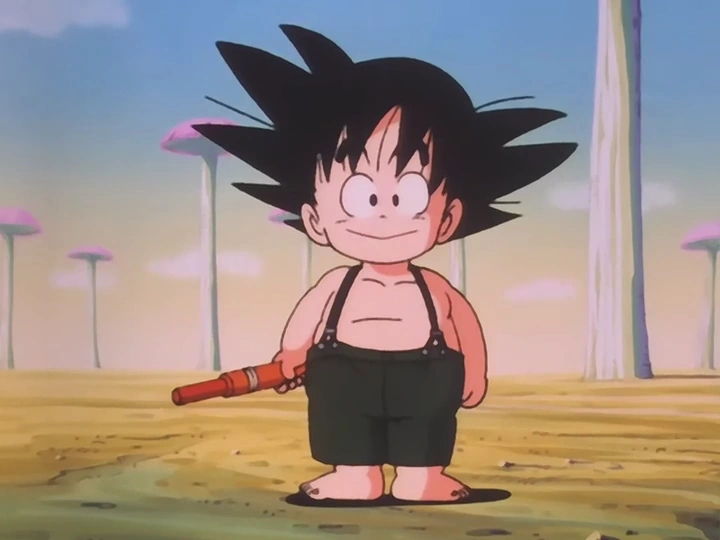 Goku stands barefoot in the desert, smiling innocently while holding his Power Pole. He wears suspenders and shorts, with a whimsical background of mushroom-shaped trees under a soft sky.