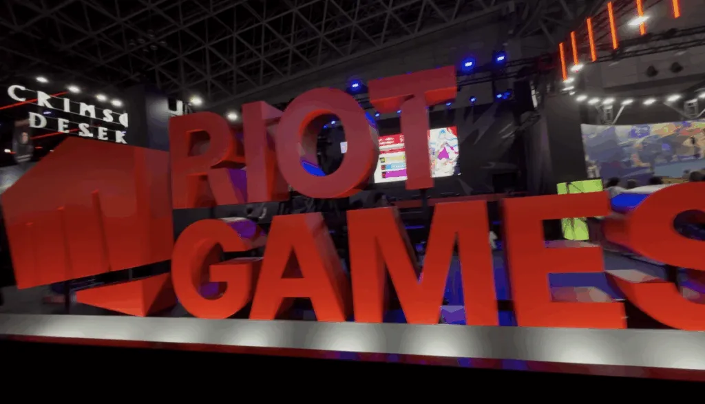 Large red “RIOT GAMES” letters stand boldly at the Riot Games booth during Tokyo Game Show 2025, surrounded by bright lights, digital screens, and a modern gaming setup inside the convention ha