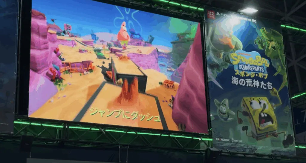 A large screen at Tokyo Game Show 2025 displays gameplay from SpongeBob SquarePants: The Cosmic Shake with Japanese subtitles, next to a bright promotional poster featuring SpongeBob, Patrick, and other characters under green lights.