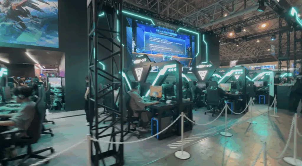Gamers sit at futuristic neon-lit stations playing demos at Tokyo Game Show 2025, surrounded by glowing teal lights, large overhead screens, and a sleek, high-tech booth setup inside the convention hall.