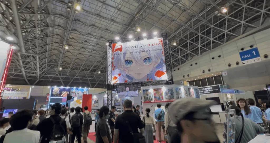 Crowds explore Tokyo Game Show 2025 inside a large convention hall, featuring a massive screen displaying an anime-style character with blue eyes above several colorful game booths under the high steel roof of Hall 1.