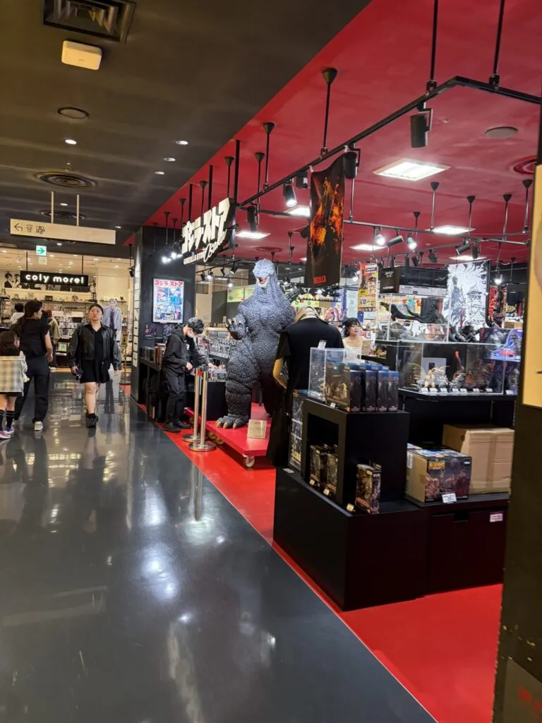 Wide view of the Godzilla Store Osaka inside Shinsaibashi PARCO, showcasing a large Godzilla statue, red and black interior design, and shelves filled with Godzilla merchandise.