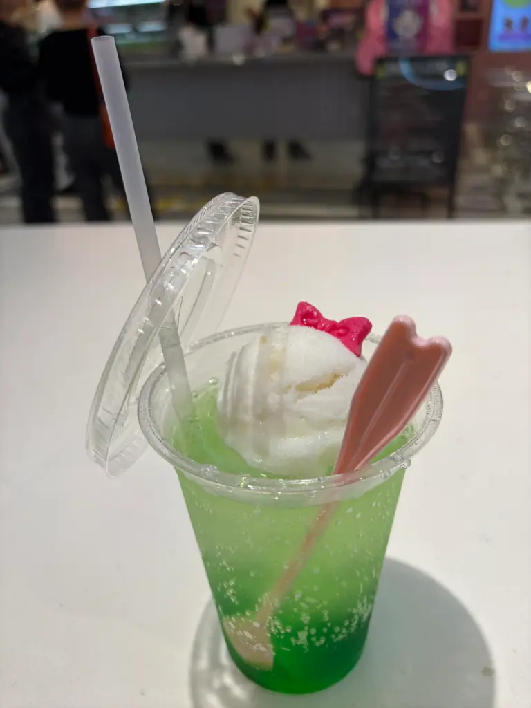Refreshing melon soda float from PINK WOO WAFFLE café topped with vanilla ice cream and a pink spoon inside a clear cup.