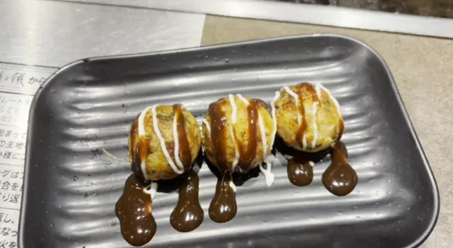Freshly cooked takoyaki topped with savory sauce and mayonnaise served on a metal tray at Takonotetsu Tsunoda in Osaka.
