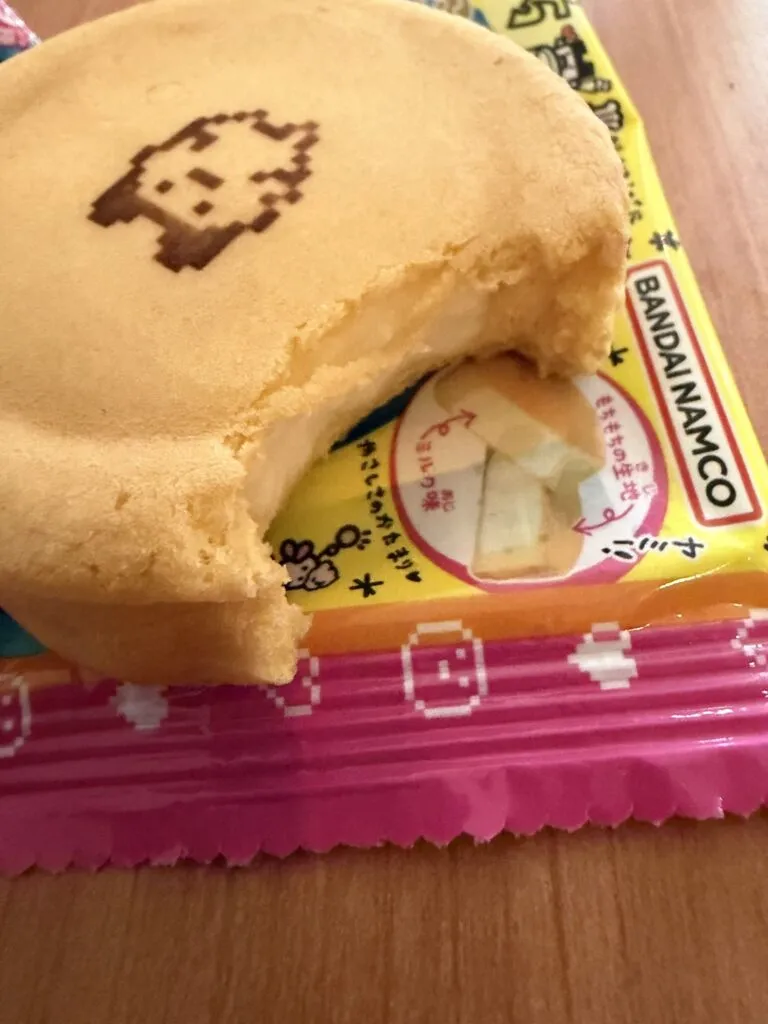 A Tamagotchi Manmaruyaki dessert with a bite taken out, showing the creamy milk filling inside the soft golden dough.