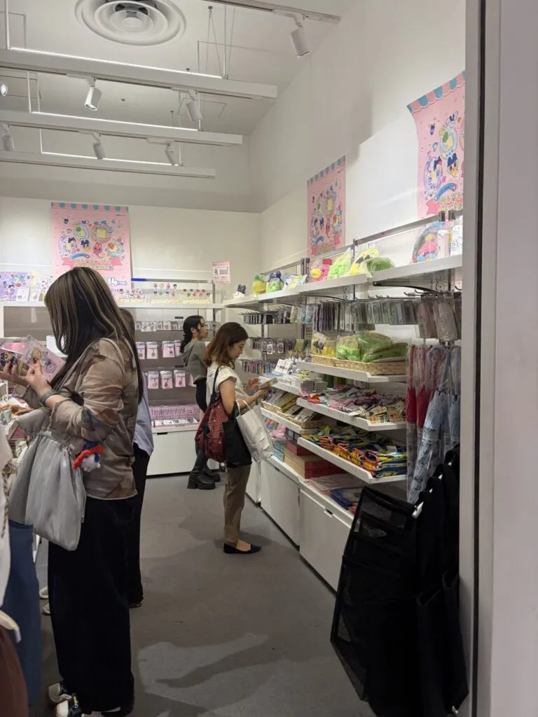 Customers and staff interacting at the checkout area surrounded by pastel Tamagotchi displays and plushies.
