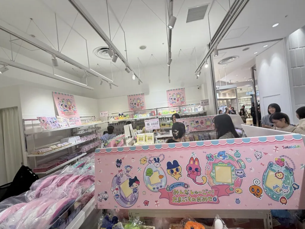 Inside the Tamagotchi pop-up store with multiple pink posters and shelves lined with plushies, keychains, and accessories.