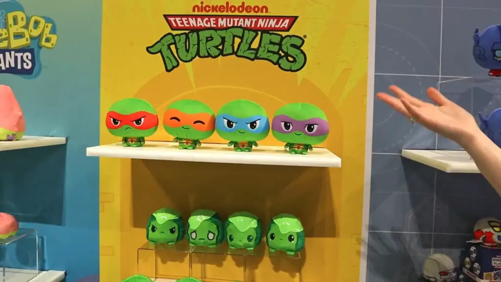 Nickelodeon Teenage Mutant Ninja Turtles reversible plushies by TeeTurtle featuring Raphael, Michelangelo, Leonardo, and Donatello with expressive faces on a yellow and blue display at Toy Fair NY 2025.