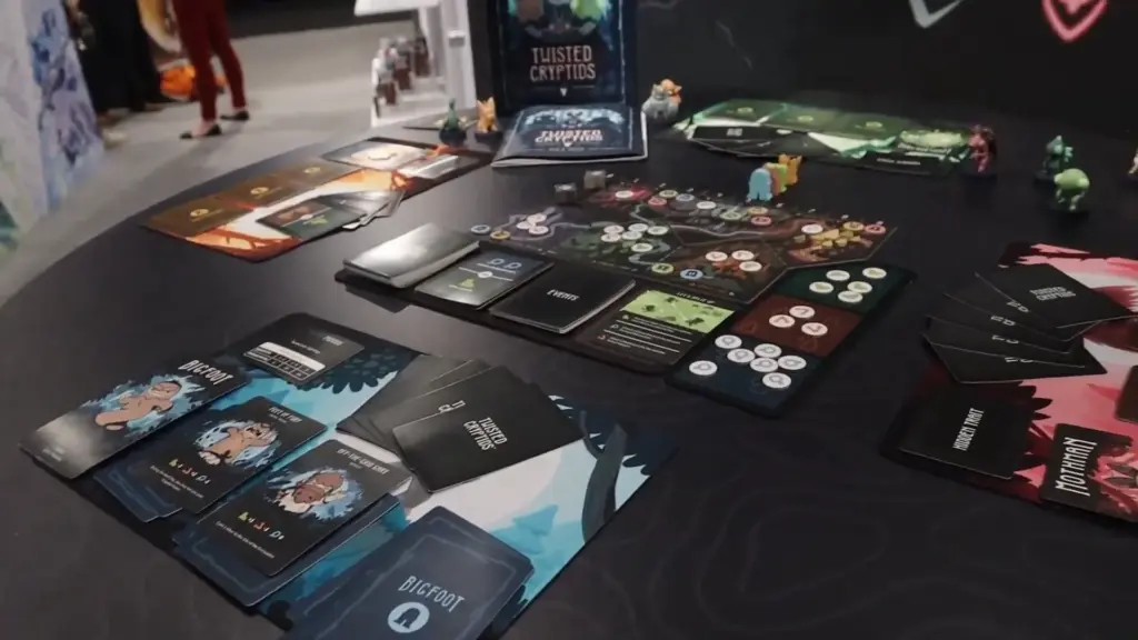 Full Twisted Cryptids game setup displayed at the Toy Fair NY 2025 Unstable Games showcase, featuring colorful cards, player boards, and mini cryptid figures.