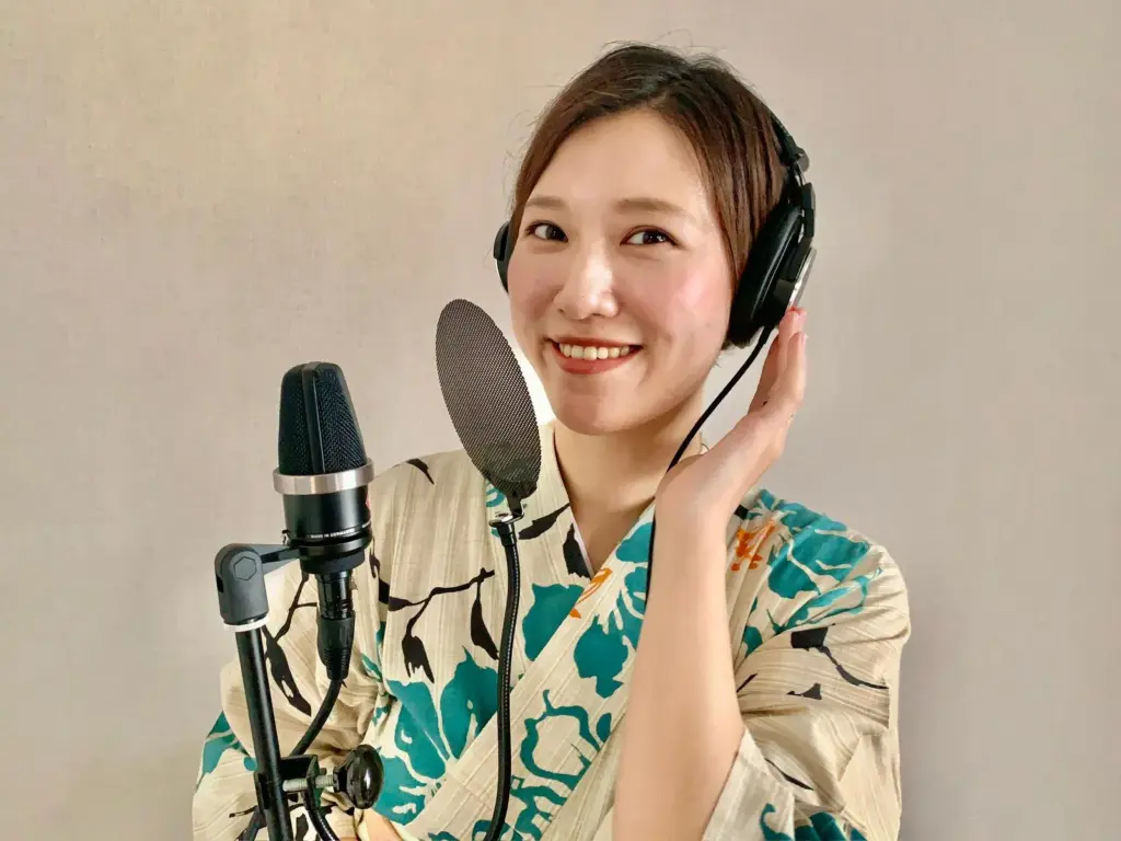 Yuui Hiromatsu, a Japanese voice actress, smiles while wearing headphones and standing in front of a microphone, dressed in a traditional yukata.