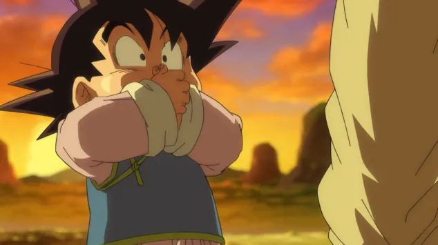 Young Goten covering his mouth with both hands in shock, standing against a glowing sunset sky with rocky cliffs in the distance while facing an adult figure just off-screen.