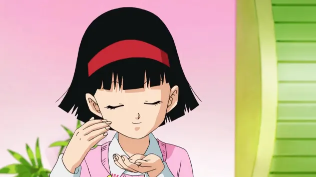 Videl gently touching her cheek with her eyes closed, smiling softly in a pastel-colored kitchen with a calm, caring expression.