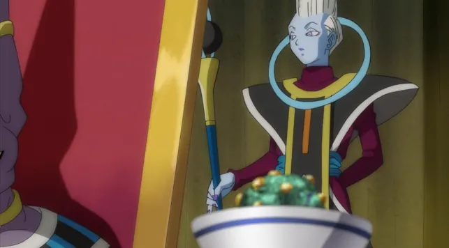 Whis standing calmly with his staff behind a bowl of colorful food, his blue ring collar glowing as he looks toward someone off-screen in an elegant room.
