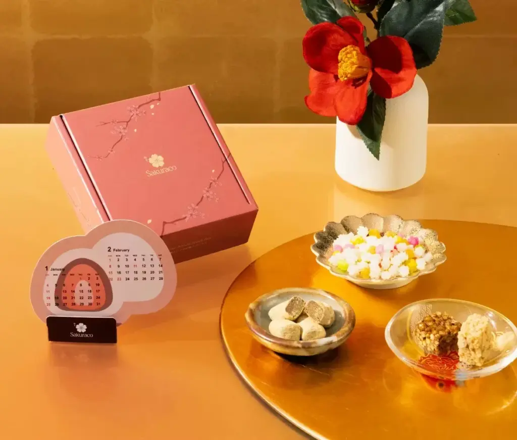 Sakuraco January 2026 Box featuring a Japanese tea ceremony setup with green tea, traditional wagashi, kagami mochi decoration, Daruma-shaped senbei, and the red Sakuraco box themed around Oshogatsu and renewal